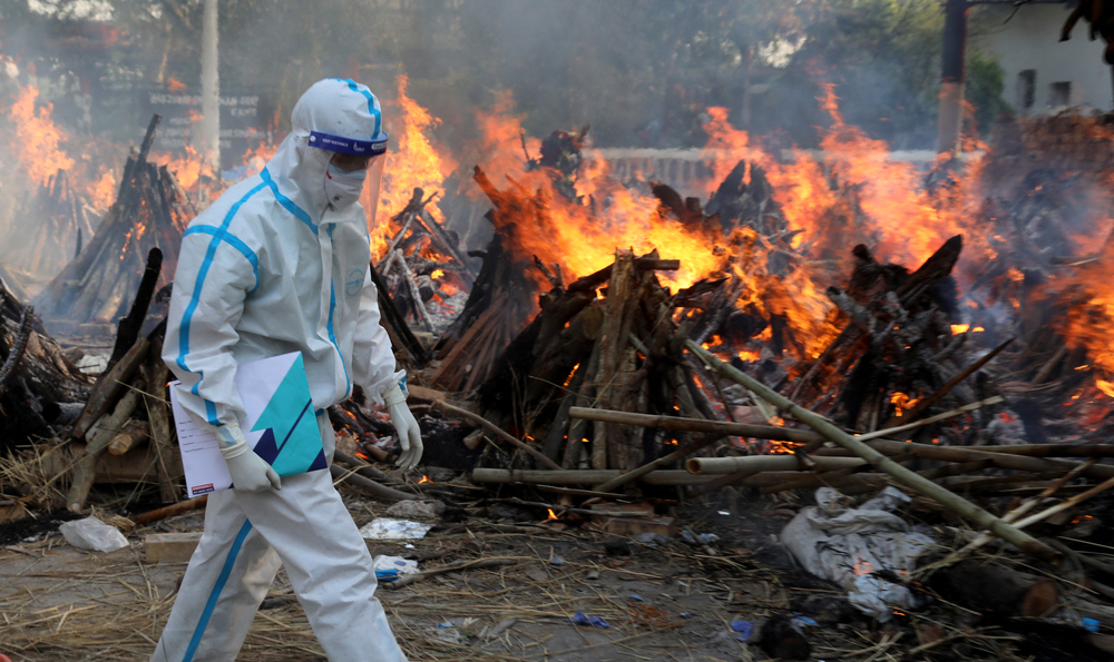 New Delhi: En pårørende iført vernutstyr under massekremering av covid-19-døde ved et krematorium i New Delhi. Foto: Shutterstock.
